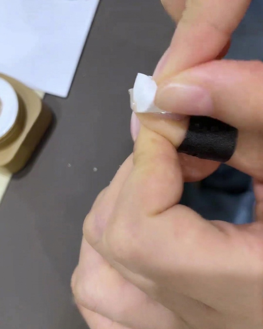 Primo piano di una mano che applica un piccolo pezzo di nastro adesivo bianco alla base della cuticola dellunghia.