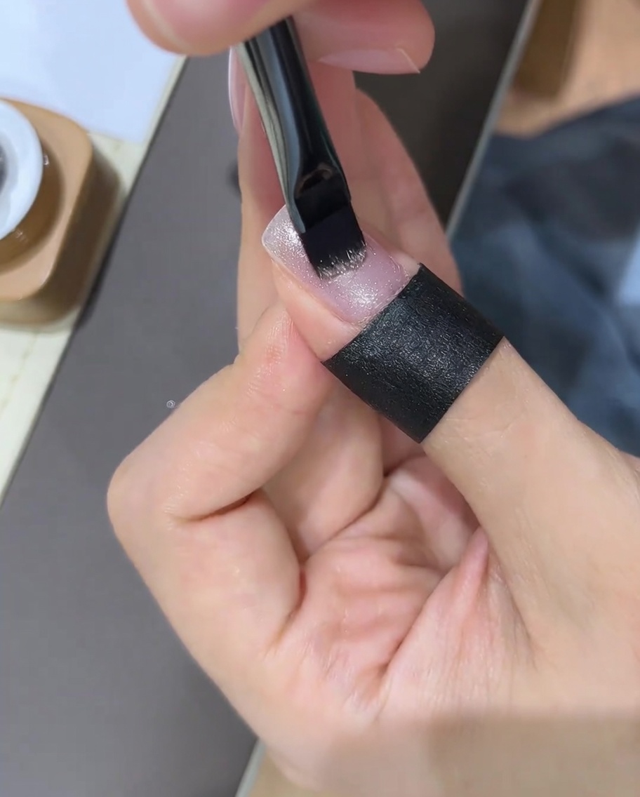Una mano che utilizza un magnete per unghie sopra ununghia appena smaltata per manipolare le particelle di glitter.