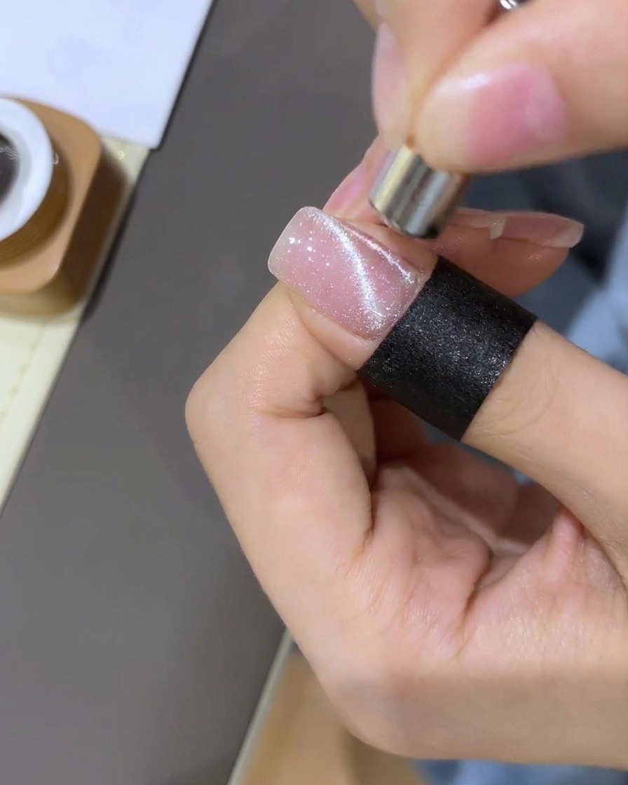 Un primo piano che mostra un magnete utilizzato per attirare il glitter magnetico in una forma sferica concentrata sullunghia.