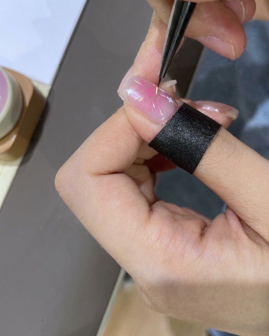 Un dotting tool utilizzato per posizionare piccoli accenti colorati attorno allunghia decorata con stelle.