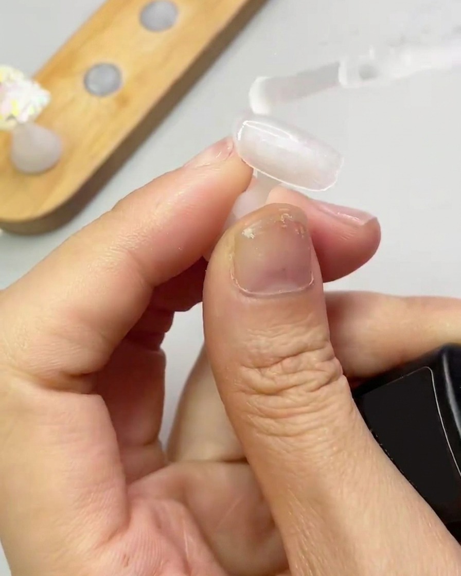 Un pennello applica uno strato sottile e trasparente di gel di rinforzo sulla punta dellunghia.