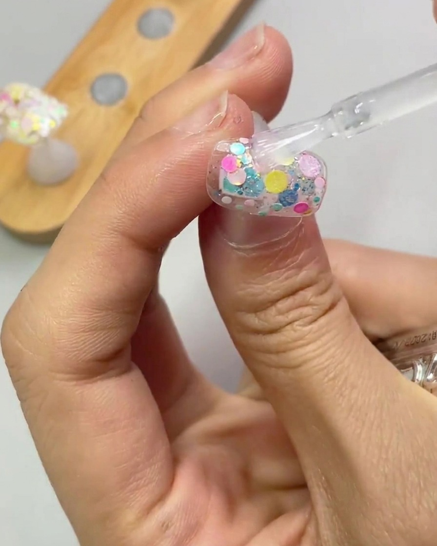 Un pennello applica uno strato trasparente di gel di rinforzo su ununghia decorata con glitter.