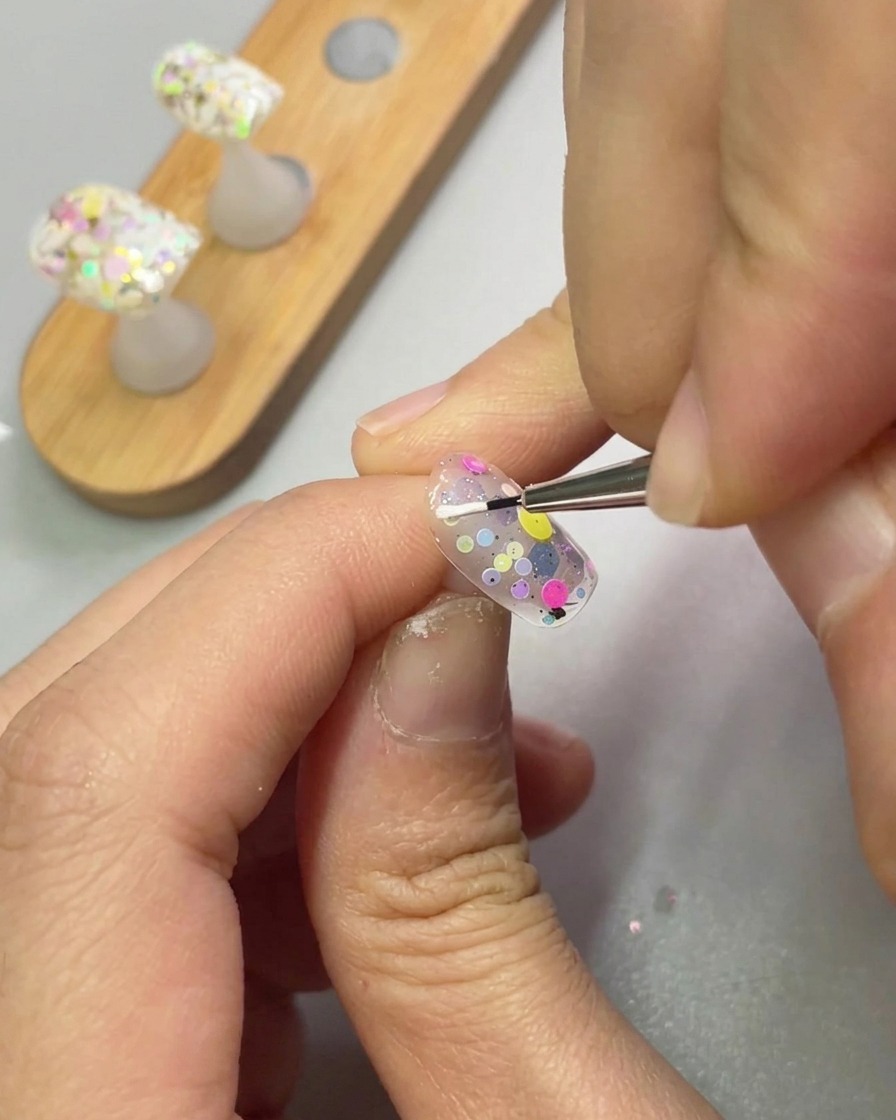 Un pennello a punta fine applica gel scultoreo bianco per creare una forma a petalo su ununghia.