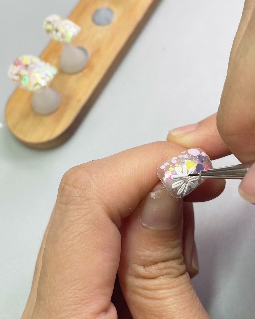 Una vista ravvicinata di un pennello che usa gel scultoreo bianco per formare i petali di una seconda piccola margherita sulla superficie dellunghia.