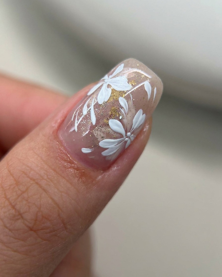 Primo piano di ununghia con un velo di rosa nude coperta da uno strato sottile di glitter oro.