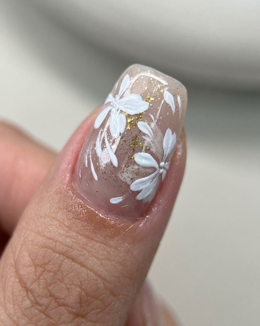 Un pennello applica il top coat trasparente su ununghia decorata con fiori e oro.