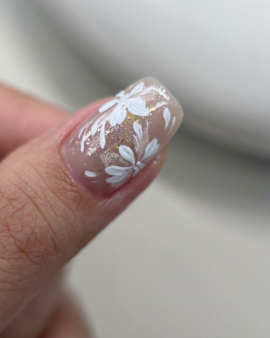Primo piano di un pennello liner che aggiunge piccoli petali bianchi su un design floreale esistente.