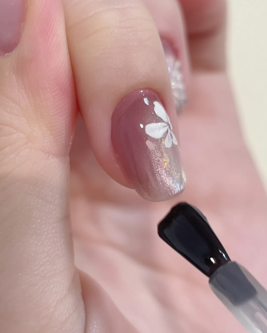 Un pennello applica un top coat lucido su una decorazione finita con gel cat-eye e fiori.
