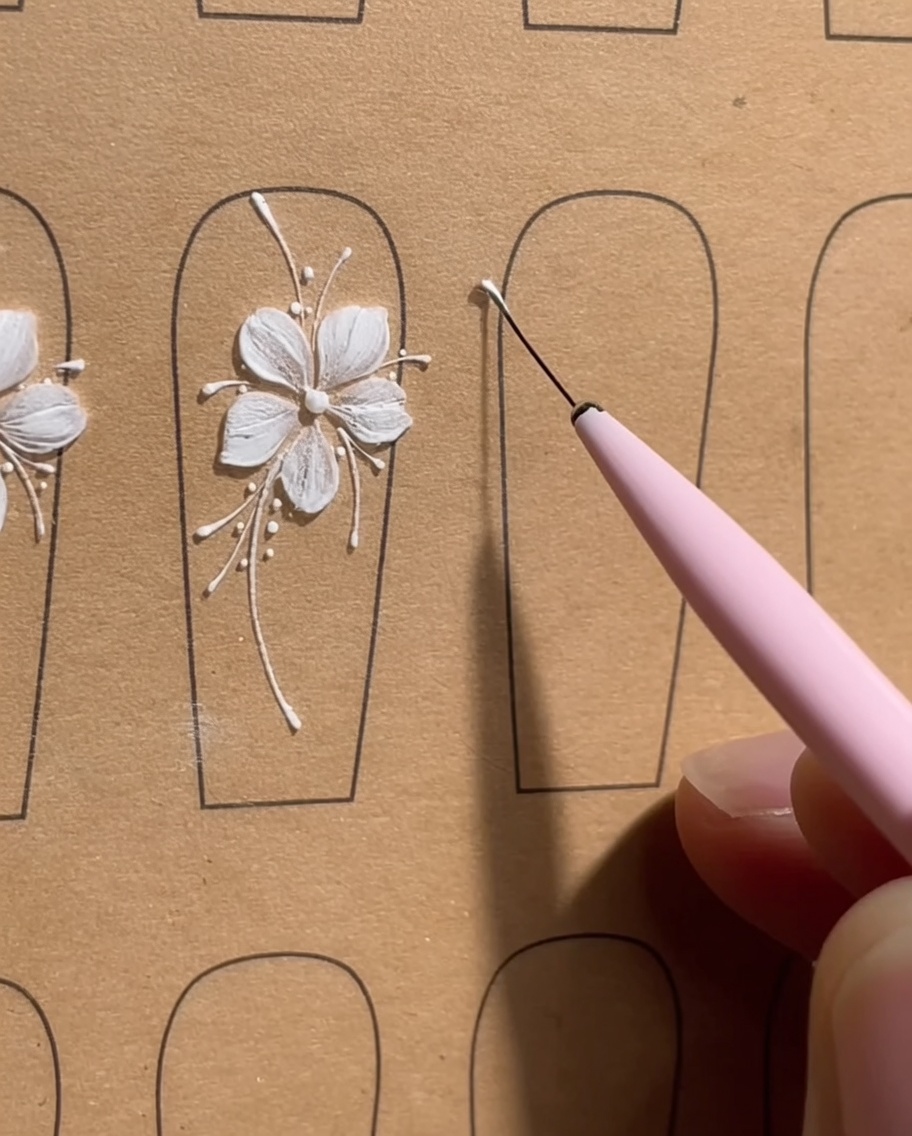 Primo piano di una tip per unghie che mostra cinque punti precisi di gel bianco disposti in un piccolo cerchio, come guida per un fiore a cinque petali.