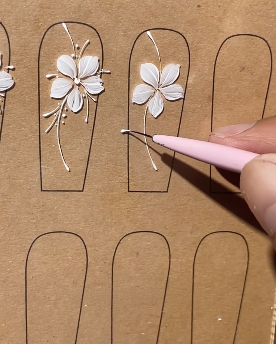 Dettaglio ravvicinato che mostra un pennello liner mentre aggiunge linee bianche lunghe e delicate tra i petali di un fiore dipinto.