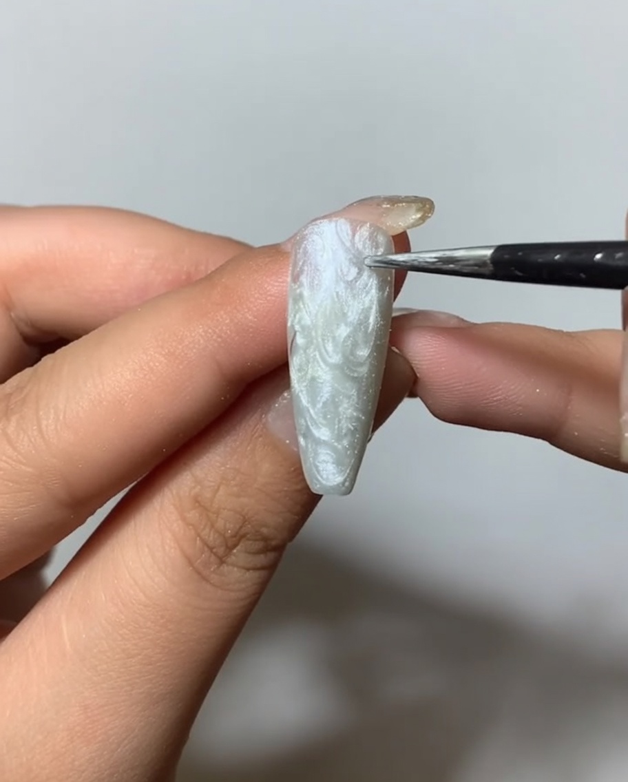 Un pennello che applica un top coat opaco trasparente su una superficie ungueale texturizzata con spider gel argento.