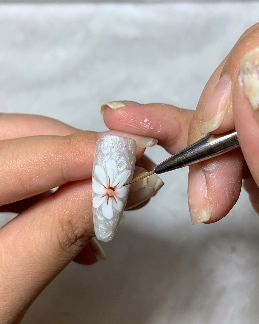 Un pennello fine che applica un gel trasparente denso sopra il design del petalo bianco sullunghia per creare dimensione.
