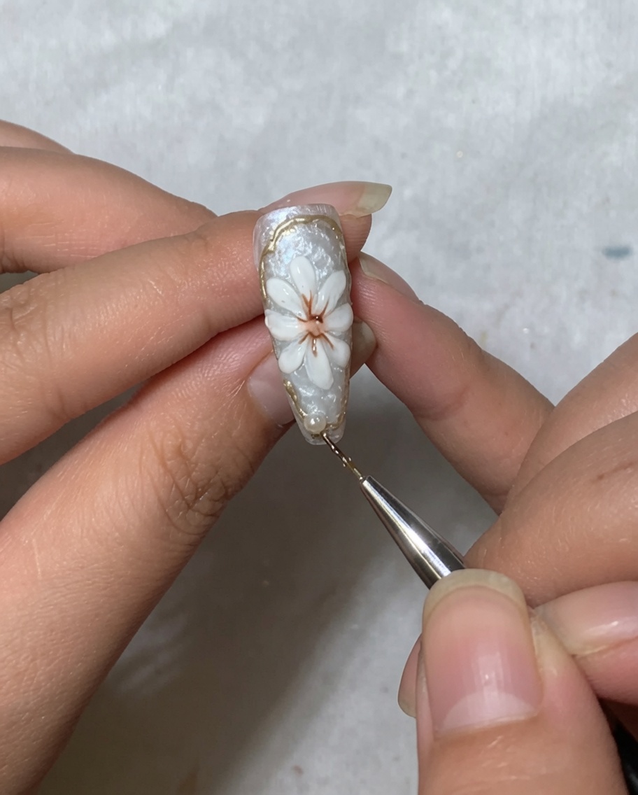 Uno strumento per nail art che posiziona una piccola perlina bianca vicino alla zona della cuticola di ununghia decorata con una margherita.