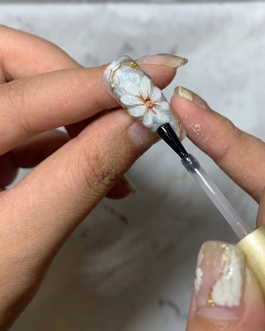 Un pennello che applica un top coat lucido finale su un design di nail art margherita 3D.