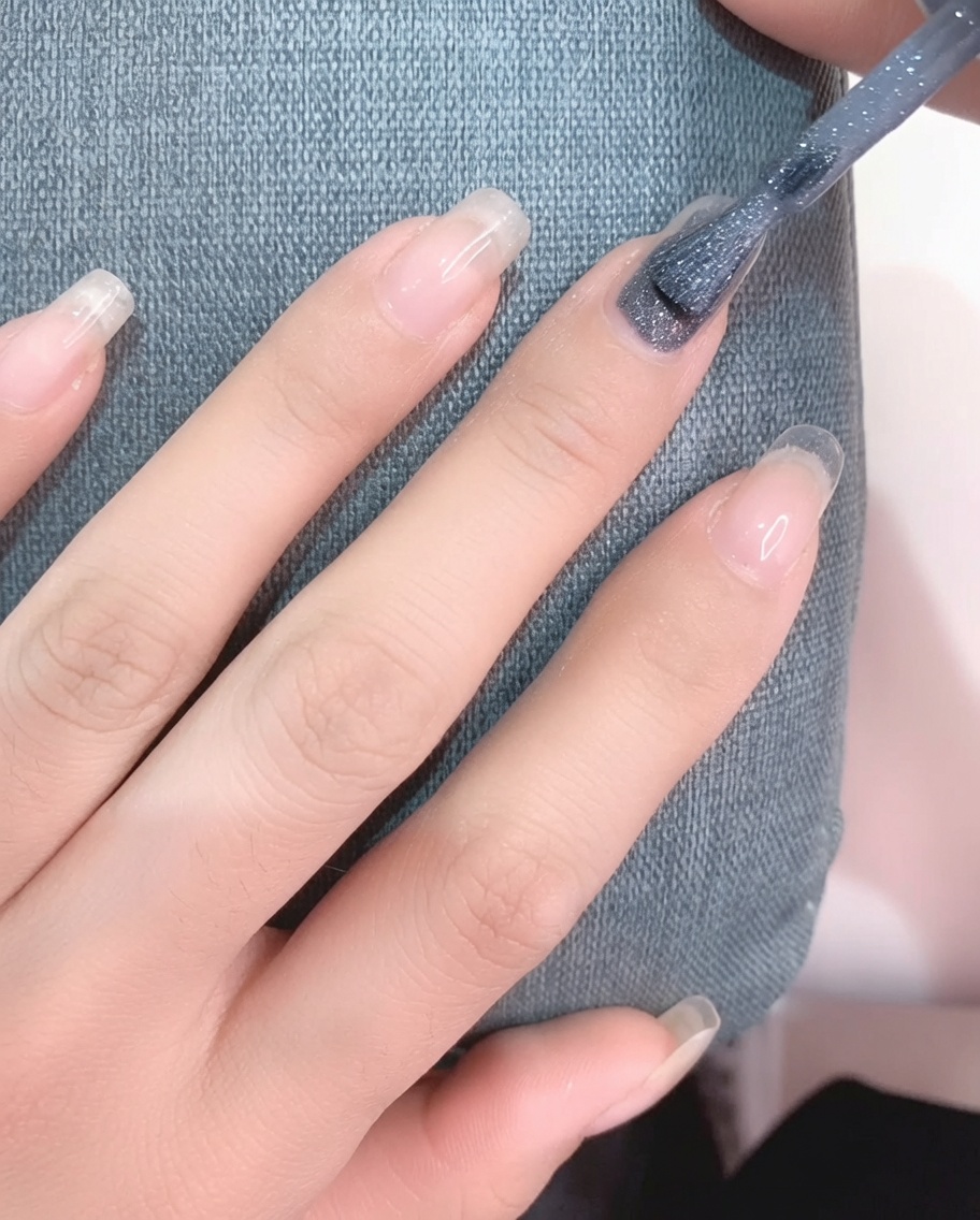 Primo piano di un pennello che applica smalto gel grigio chiaro su ununghia pulita.