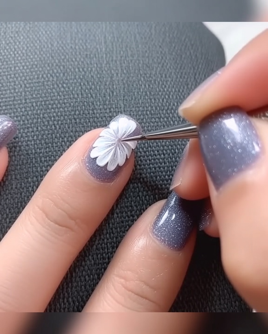 Primo piano di un pennello a punta fine che applica un piccolo punto di gel nero al centro di una margherita bianca su una base grigia.