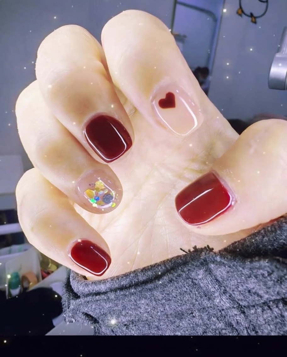 Pinzette che posizionano un piccolo charm a cuore rosso sulla superficie di ununghia coperta di gel.