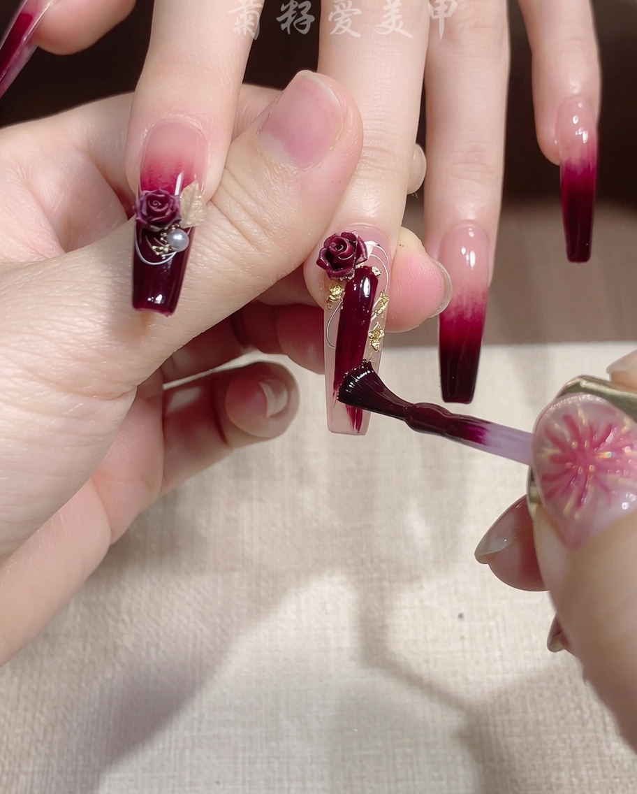 Un pennello sottile applica una scia di gel glitter oro scintillante su ununghia rossa.