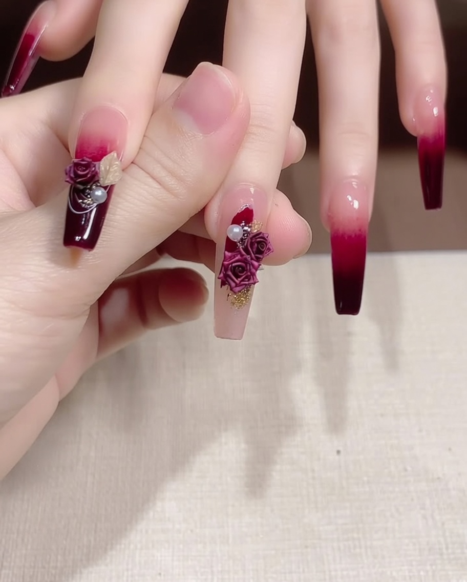 Una pinzetta posiziona una piccola perla e un elemento decorativo oro accanto a una rosa su ununghia decorata.