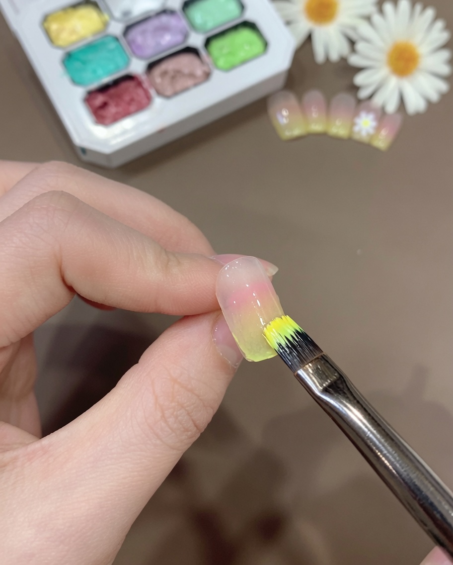 Un pennello che applica un sottile strato di miscela gel giallo trasparente sulla punta di ununghia sfumata.