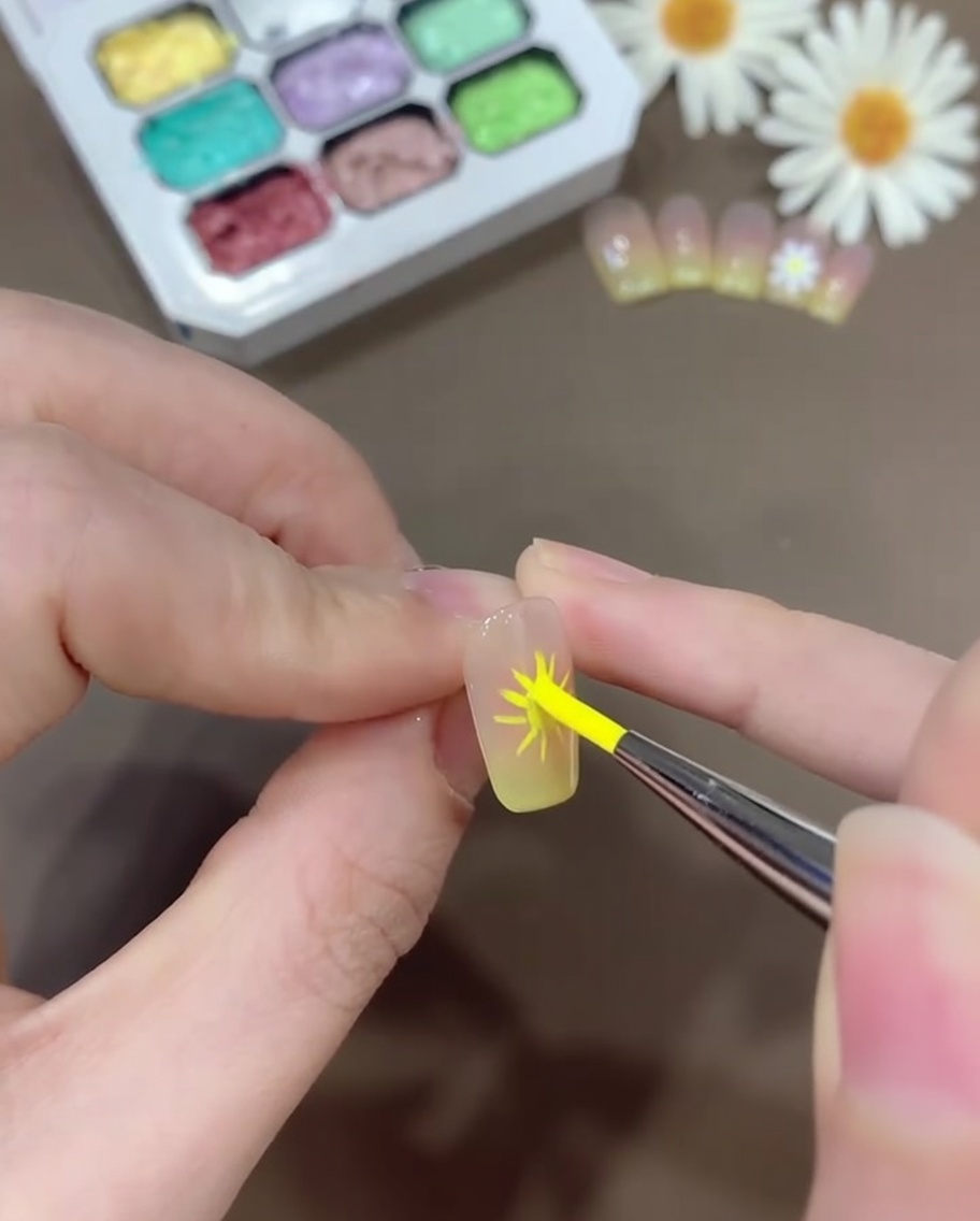 Un pennello per nail art che applica gel bianco per formare petali arrotondati, simili a quelli di una margherita, sopra le linee guida tracciate.