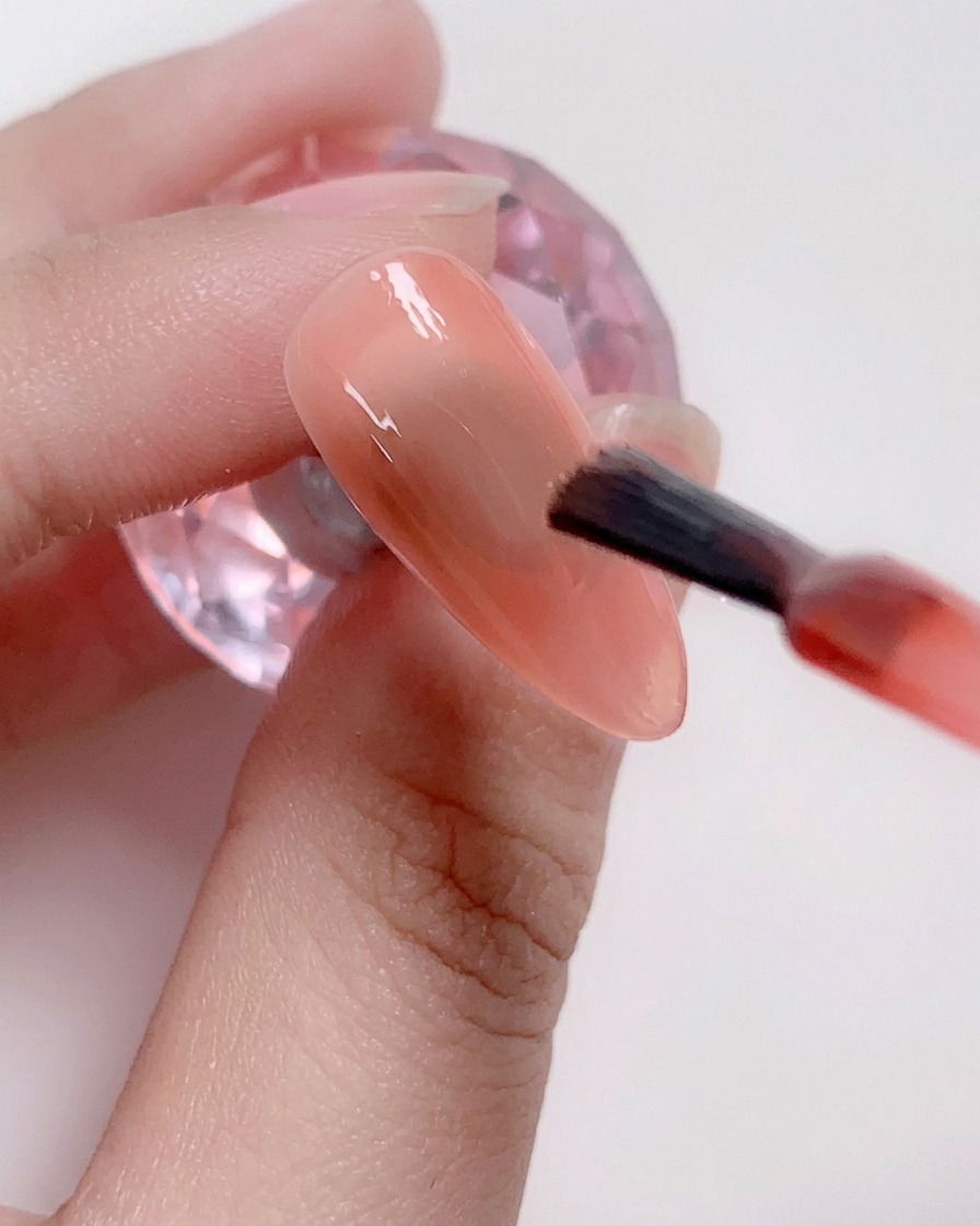 Un pennello applica uno strato di smalto gel rosa tenue al centro dellunghia.
