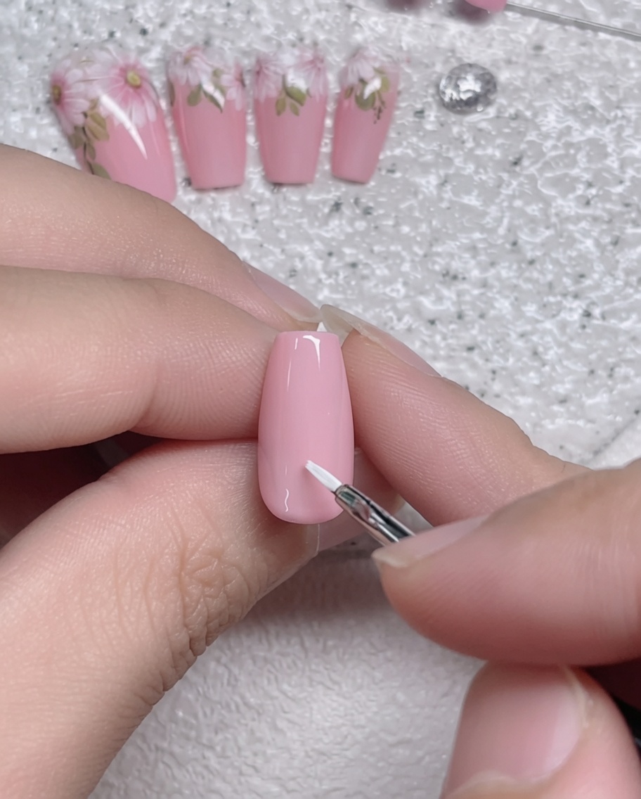 Primo piano di un pennello a punta sottile che applica una singola pennellata di bianco su ununghia con base in gel rosa.