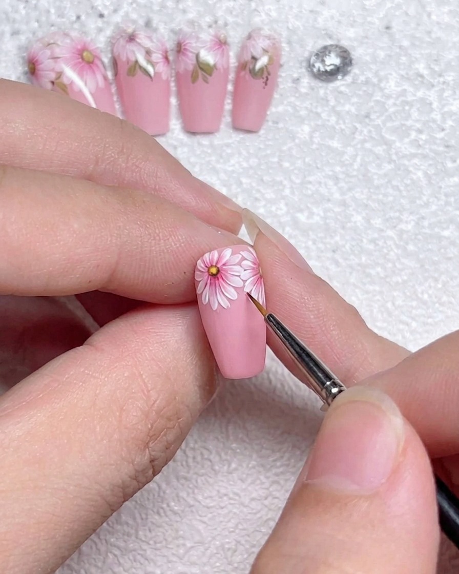 Primo piano di un pennello a punta sottile che applica precise linee di luce bianca sui bordi dei petali della margherita.