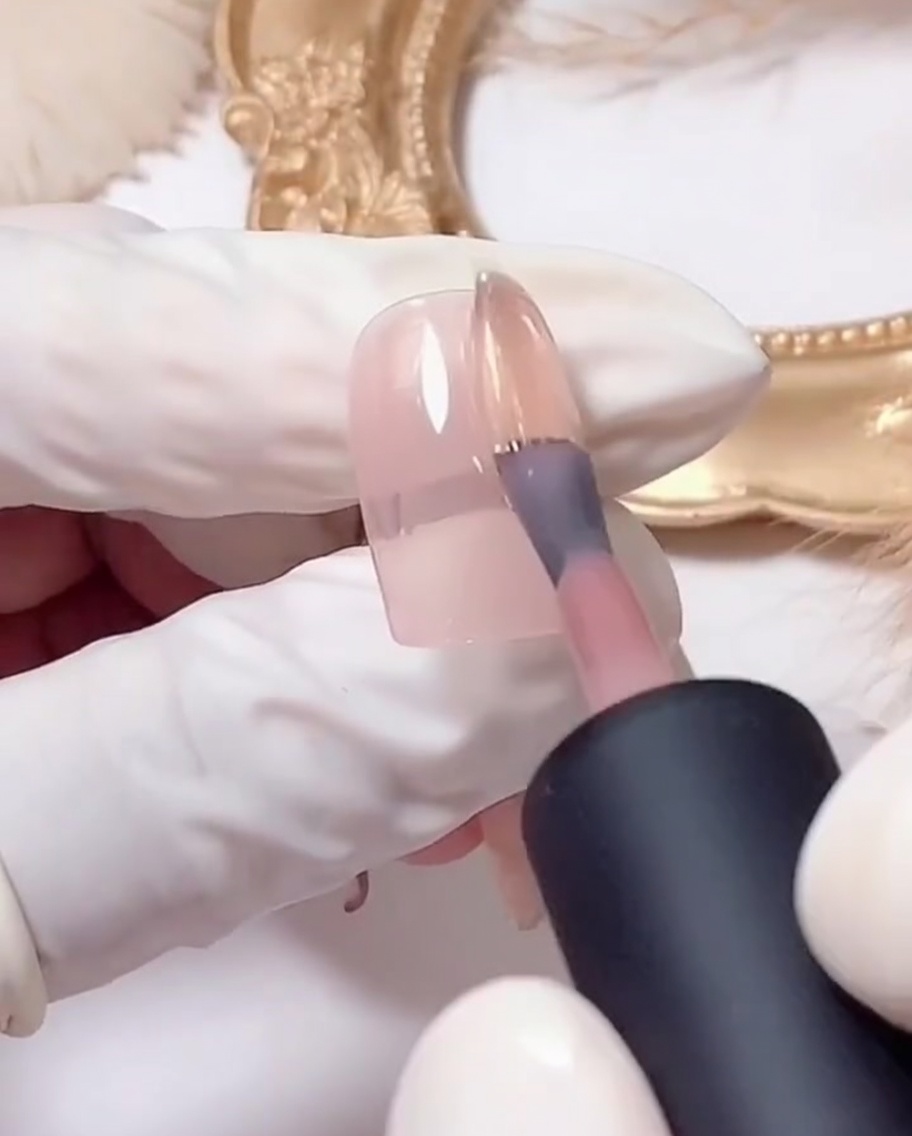 Un pennello piatto deposita il gel glitter argento sulla punta di ununghia rosa.