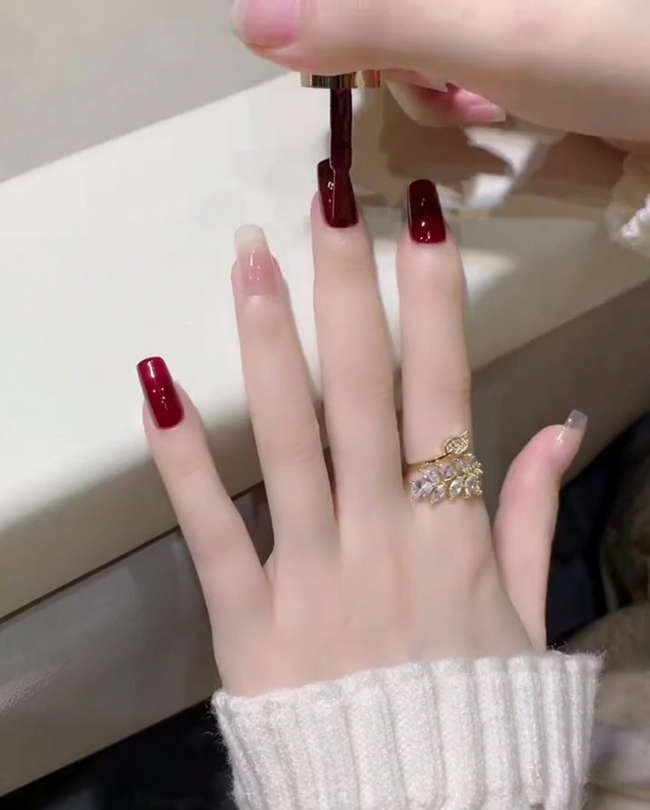 Un primo piano dellapplicazione di uno smalto gel rosso vino scuro con un pennello su ununghia del pollice.