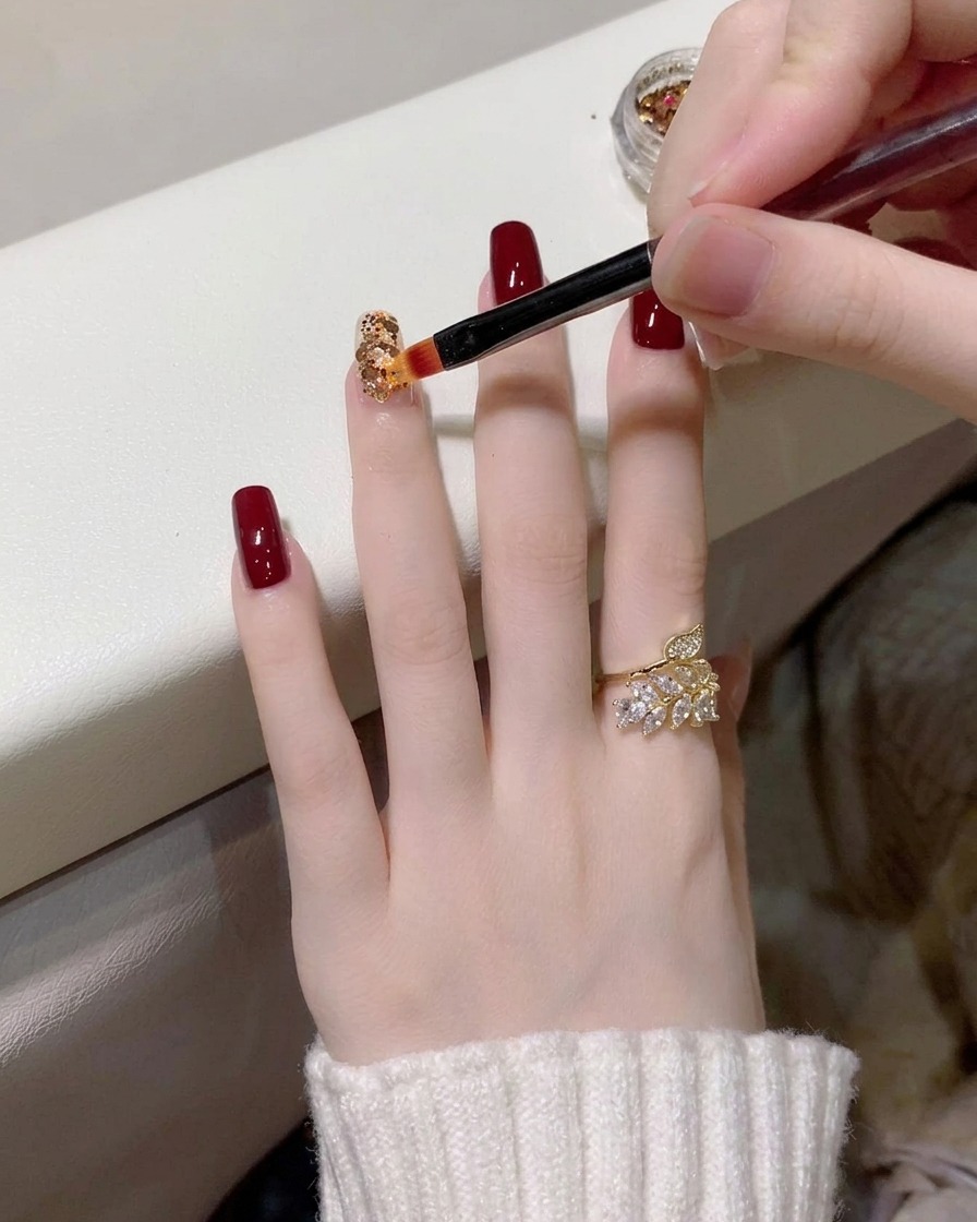Un primo piano di un pennello di precisione che posiziona glitter oro e olografici su ununghia con base trasparente.