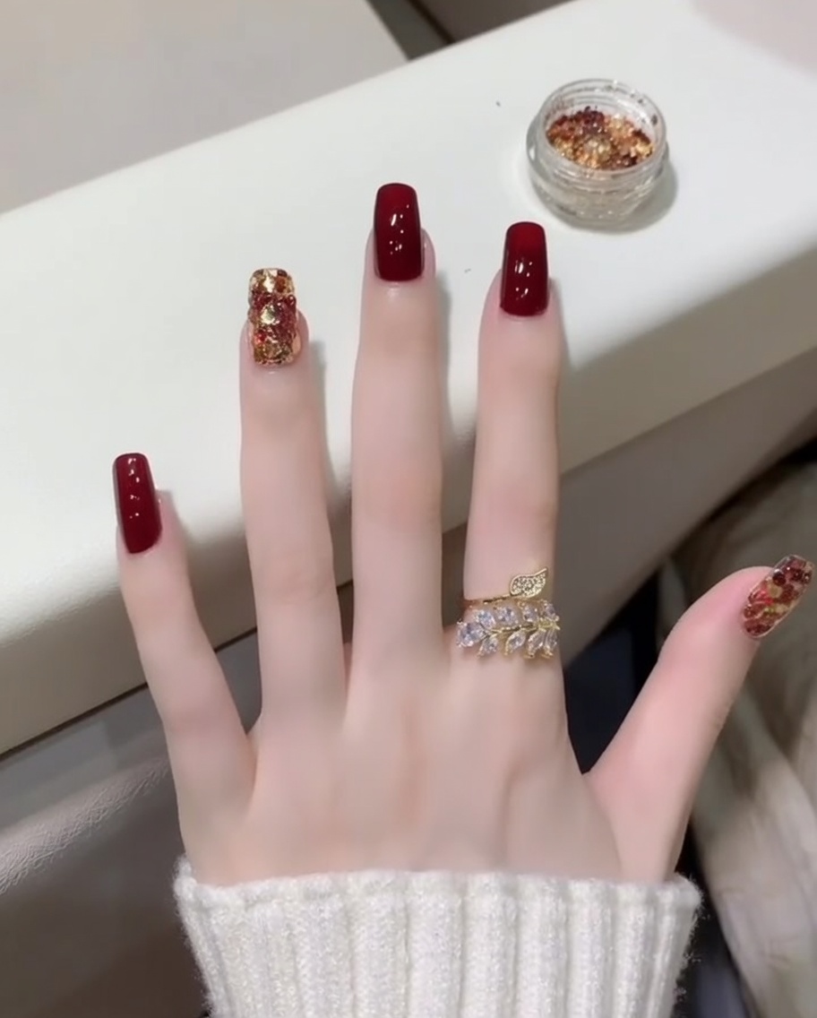 Un primo piano di un pennello che applica un top coat trasparente e lucido sopra le unghie rosso scuro e glitterate.