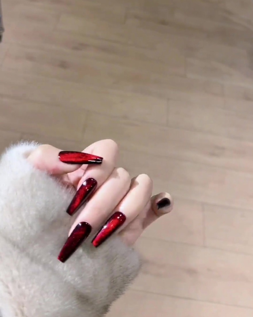 Un magnete posizionato sopra ununghia coperta da smalto magnetico rosso umido per formare una linea.