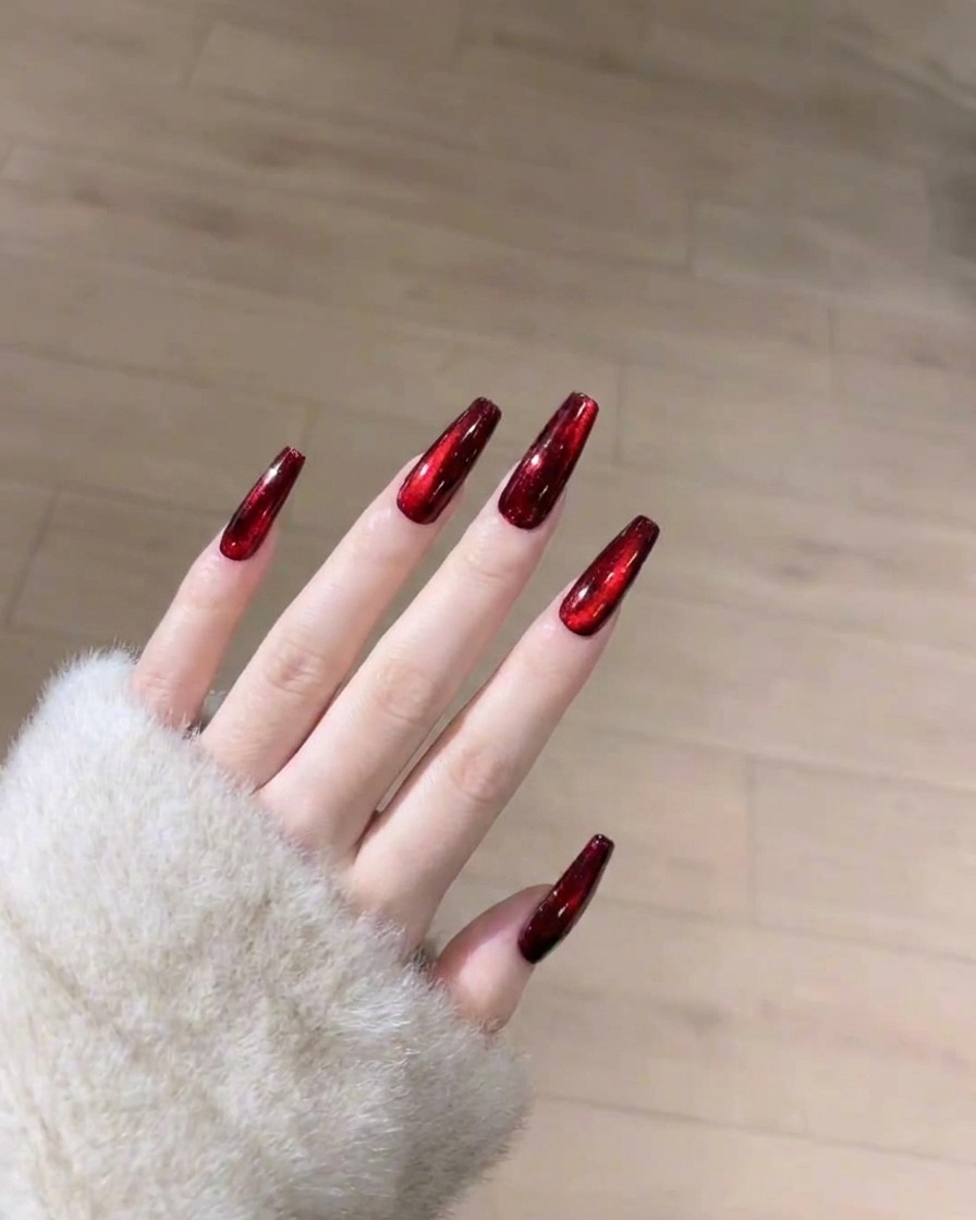 Un pennello che applica uno strato liscio e trasparente di top coat lucido sullunghia cat-eye rossa.