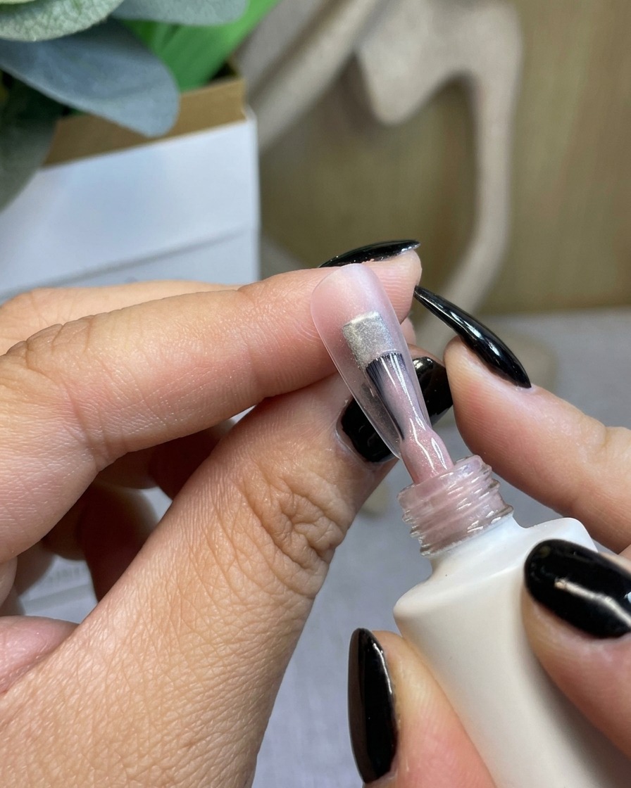 Un pennello che applica una base coat in gel trasparente e sottile su ununghia naturale.