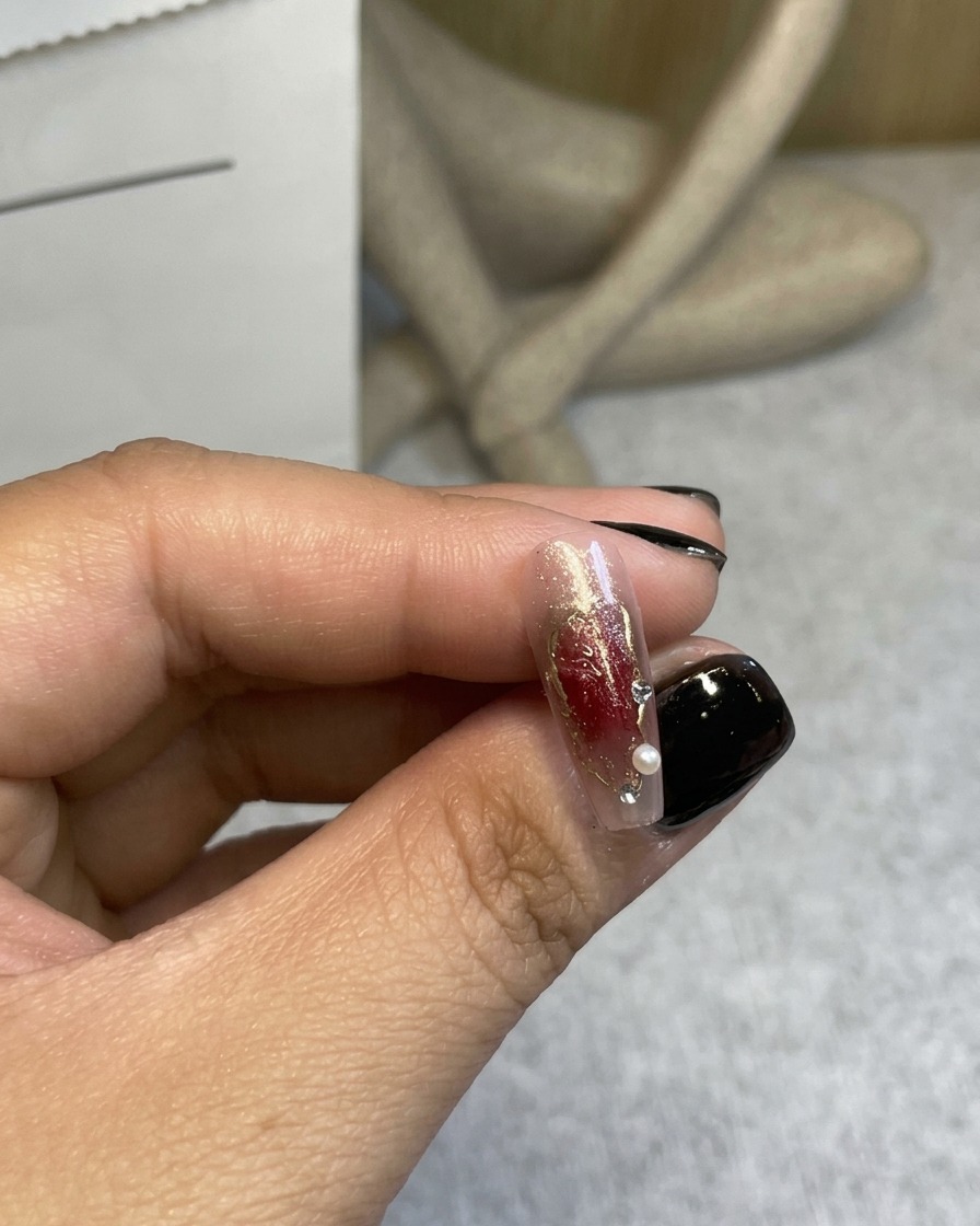 Primo piano di una rosa 3D rosso vino posizionata su ununghia decorata con lausilio di pinzette.