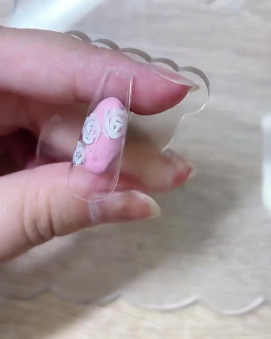 Una vista dallalto della punta dellunghia che mostra i contorni completati dei petali di rosa bianca distribuiti sulla superficie.