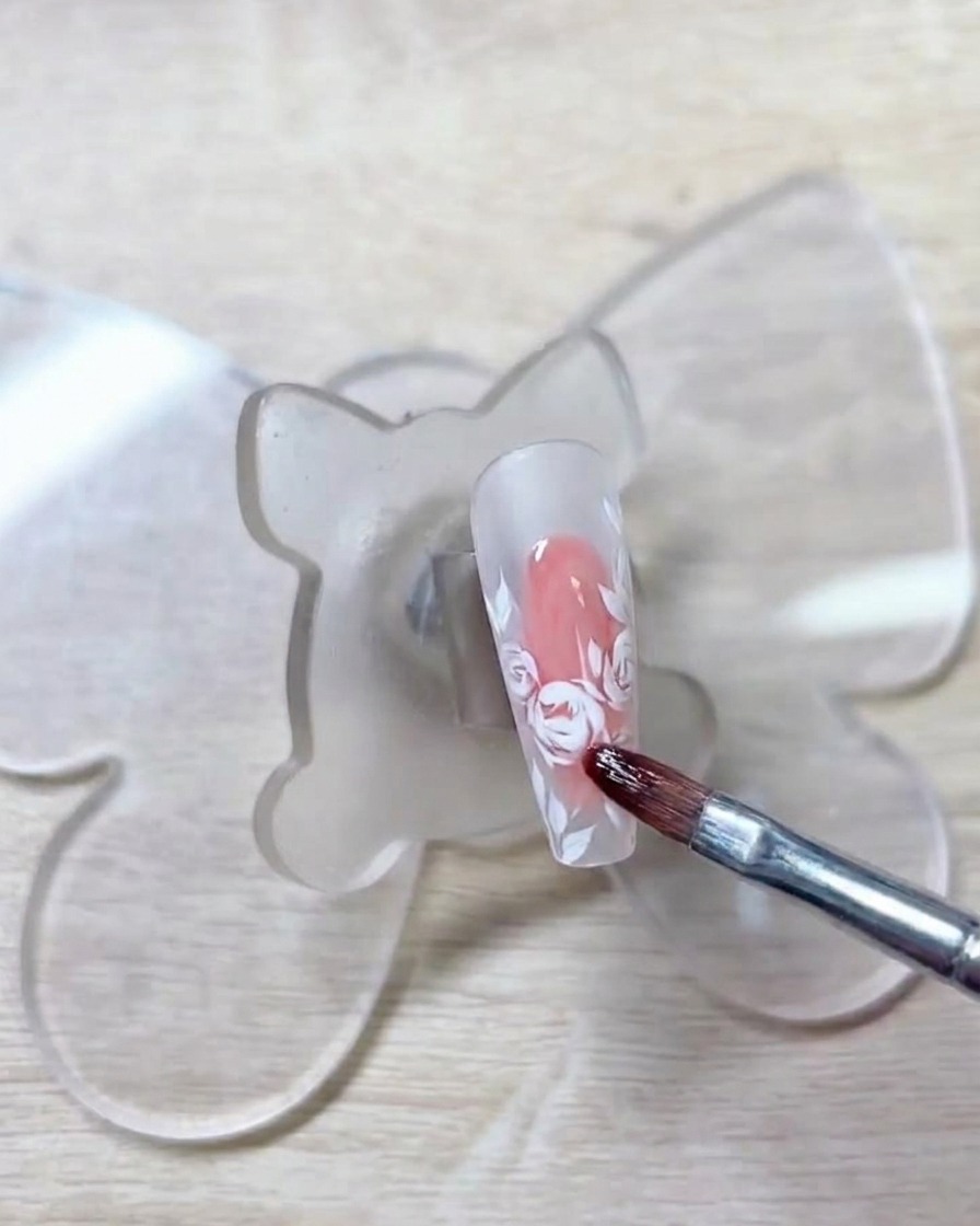 Un pennello che applica un gel rosso morbido e chiaro sui contorni delle rose bianche precedentemente disegnati.