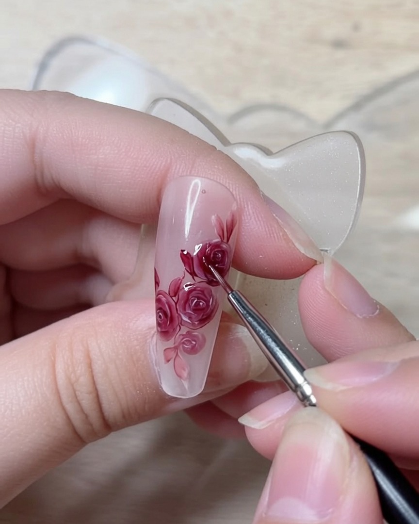 Un pennello di dettaglio fine che traccia linee rosso scuro nitide per definire le pieghe strutturali dei petali di un design di nail art con rose.