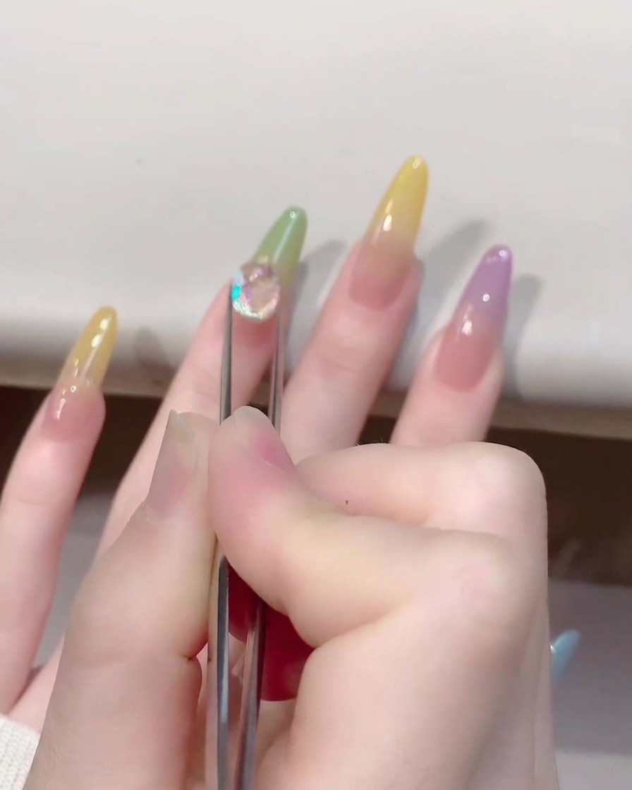 Primo piano di una pinzetta che posiziona un cristallo a forma di cuore su ununghia colorata jelly.