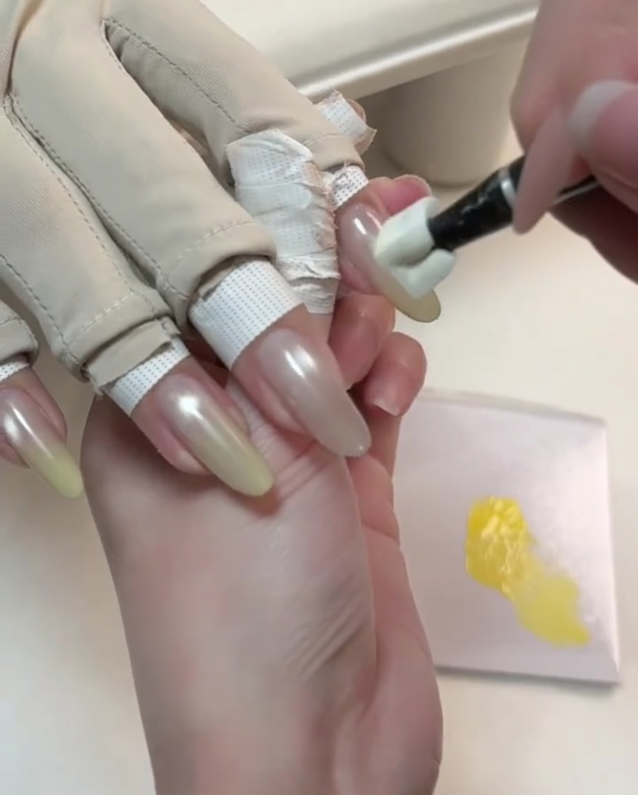 Uno strumento applica gel giallo sulla punta di ununghia nude cat-eye per iniziare la sfumatura.