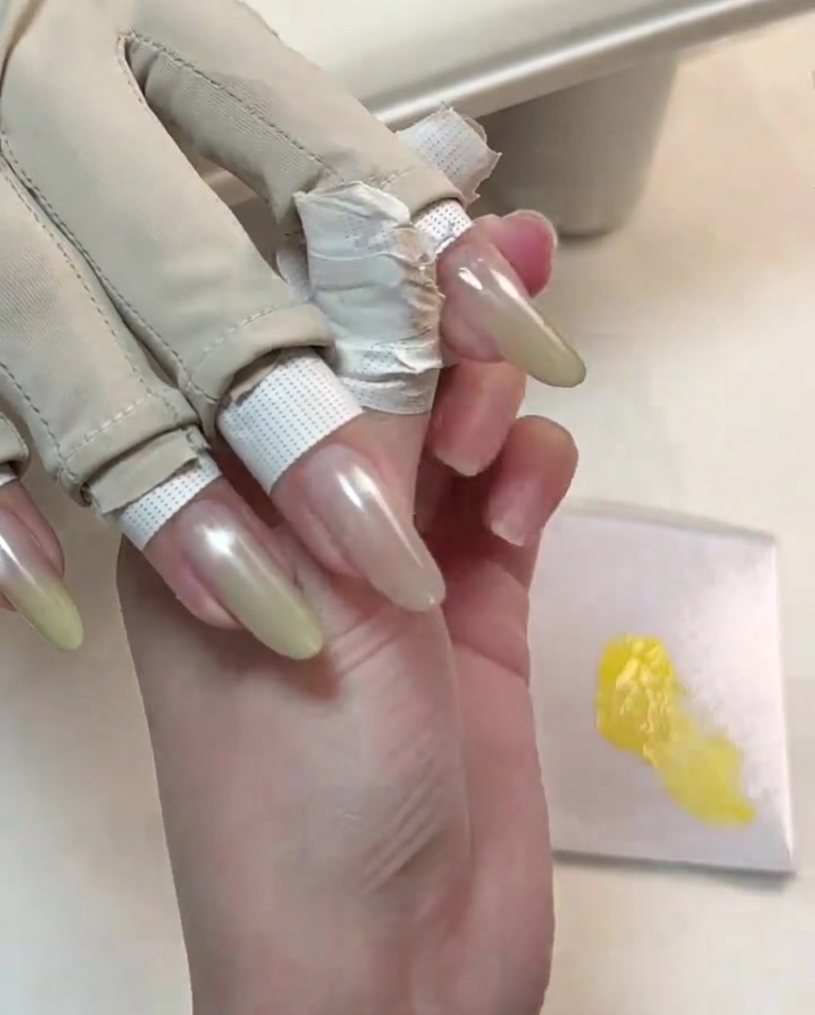 Uno strumento rifinisce il secondo strato di gel giallo sulla punta di ununghia.