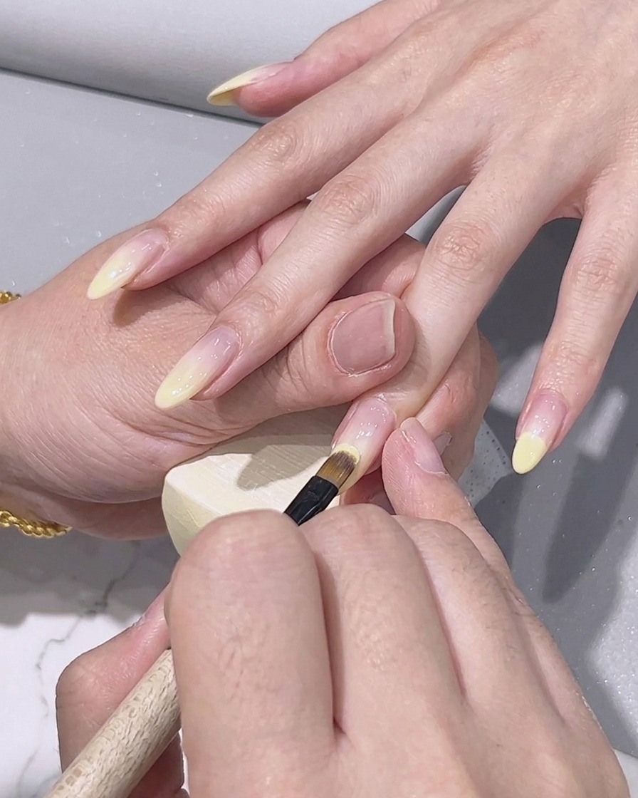 Un pennello da decorazione fine che applica il gel giallo limone sulla punta di ununghia.