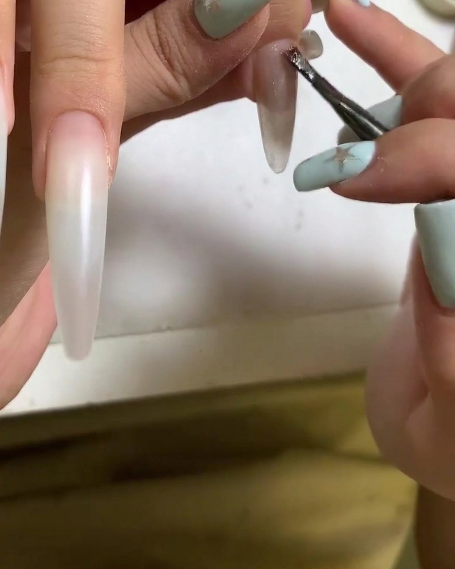 Un pennello che applica lo smalto gel cat eye sulla superficie di ununghia in acrilico.