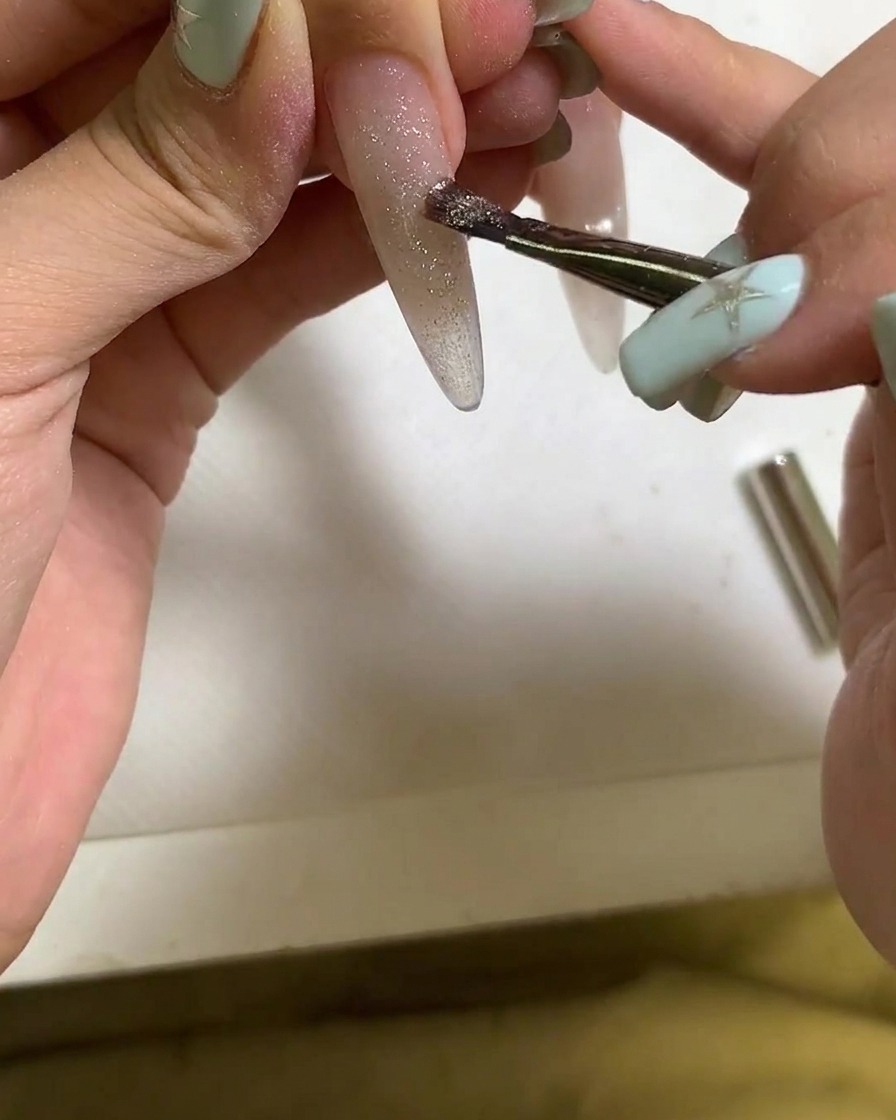 Un pennello che applica lo smalto gel cat eye su ununghia allungata.