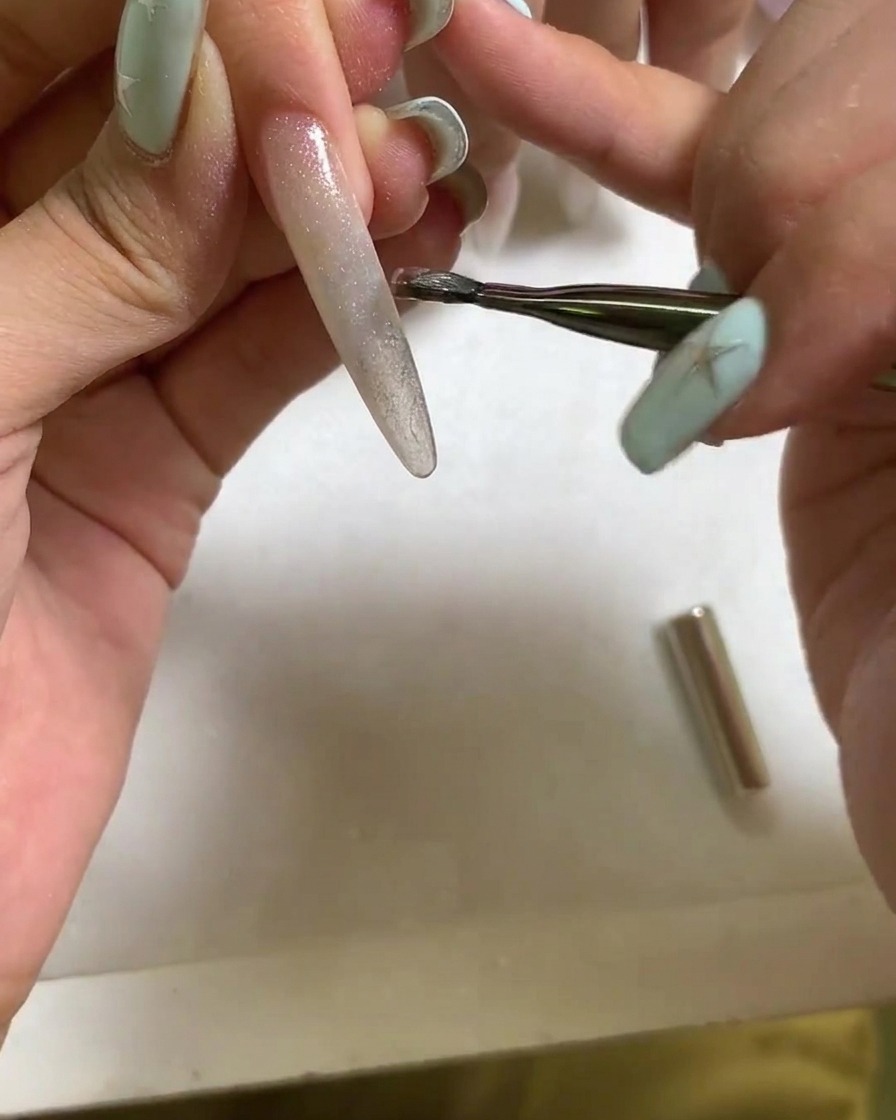 Uno strumento magnetico tenuto vicino alla superficie di ununghia in gel cat eye bagnato per formare un riflesso di luce luminoso e concentrato.