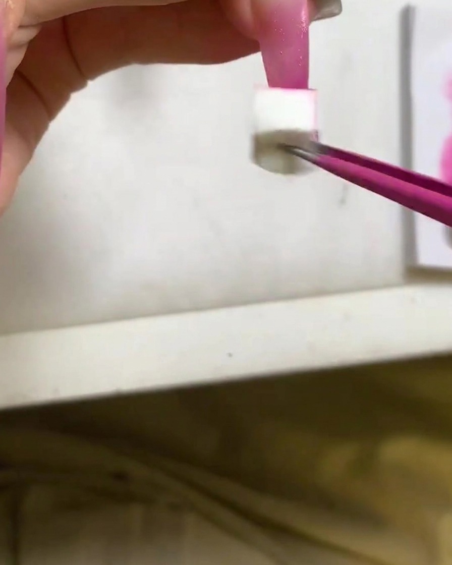 Un applicatore a spugnetta che tampona gel color rosso rosa intenso sulla punta di ununghia lunga.