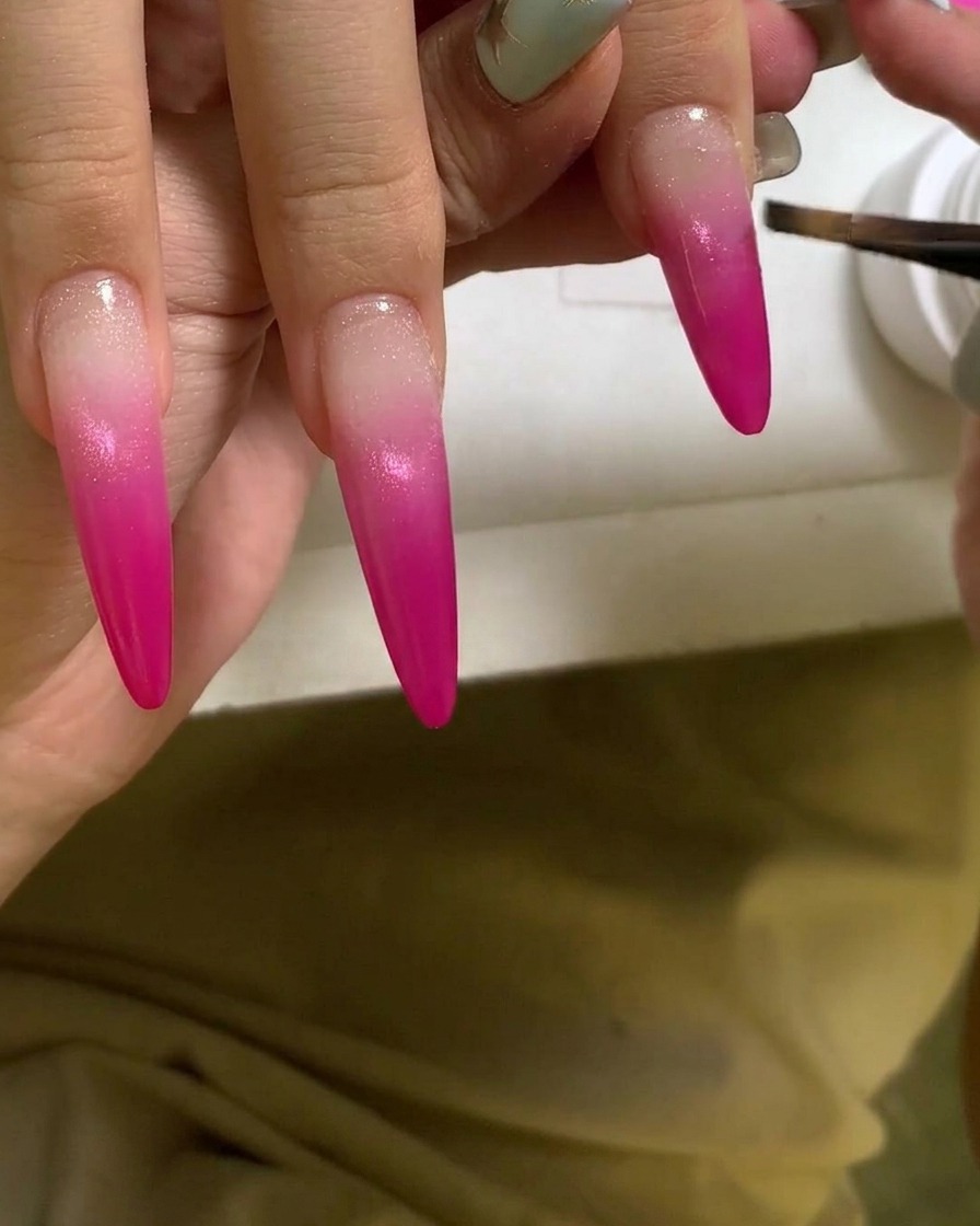 Un pennello che applica uno strato di gel trasparente e lucido su ununghia sfumata rosa vibrante.
