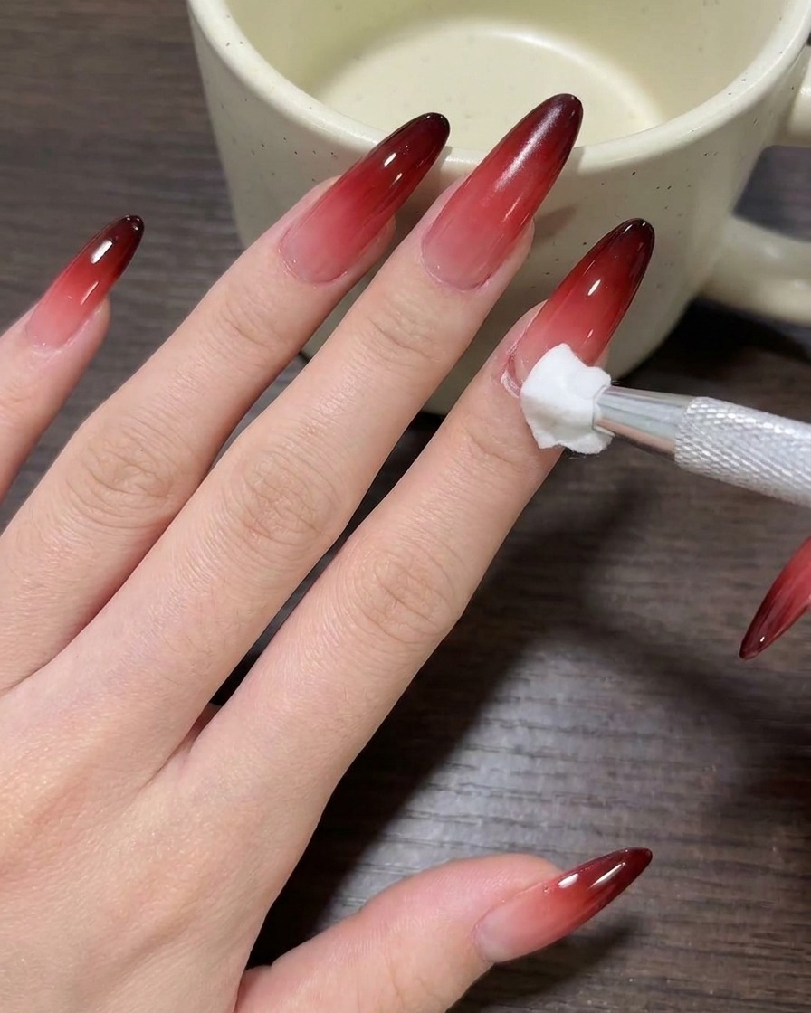 Primo piano di un pennello che applica smalto gel color carne nude su ununghia pulita.