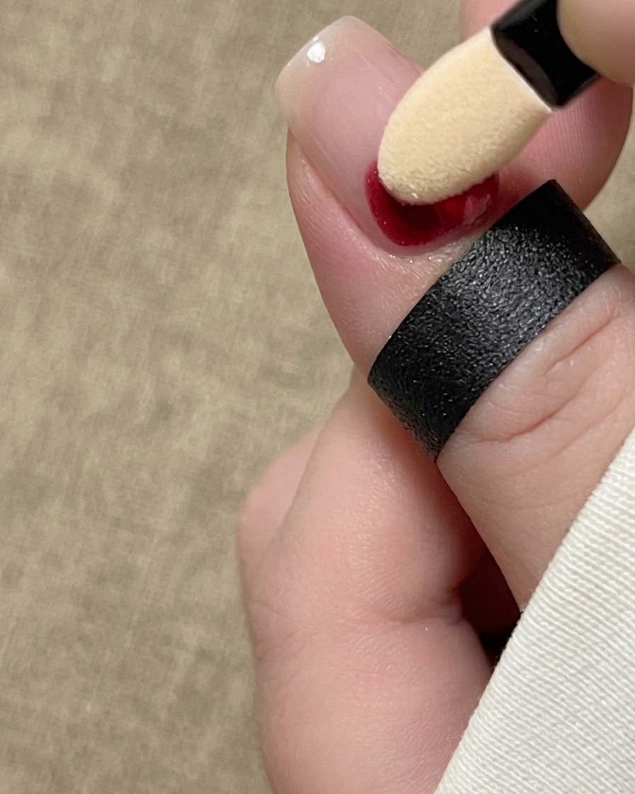 Un applicatore in spugna per ombretto che tampona pigmento in inchiostro rosso alla base di ununghia naturale.